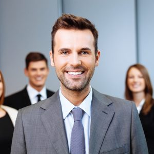 Portrait of happy team leader with group of business people in background